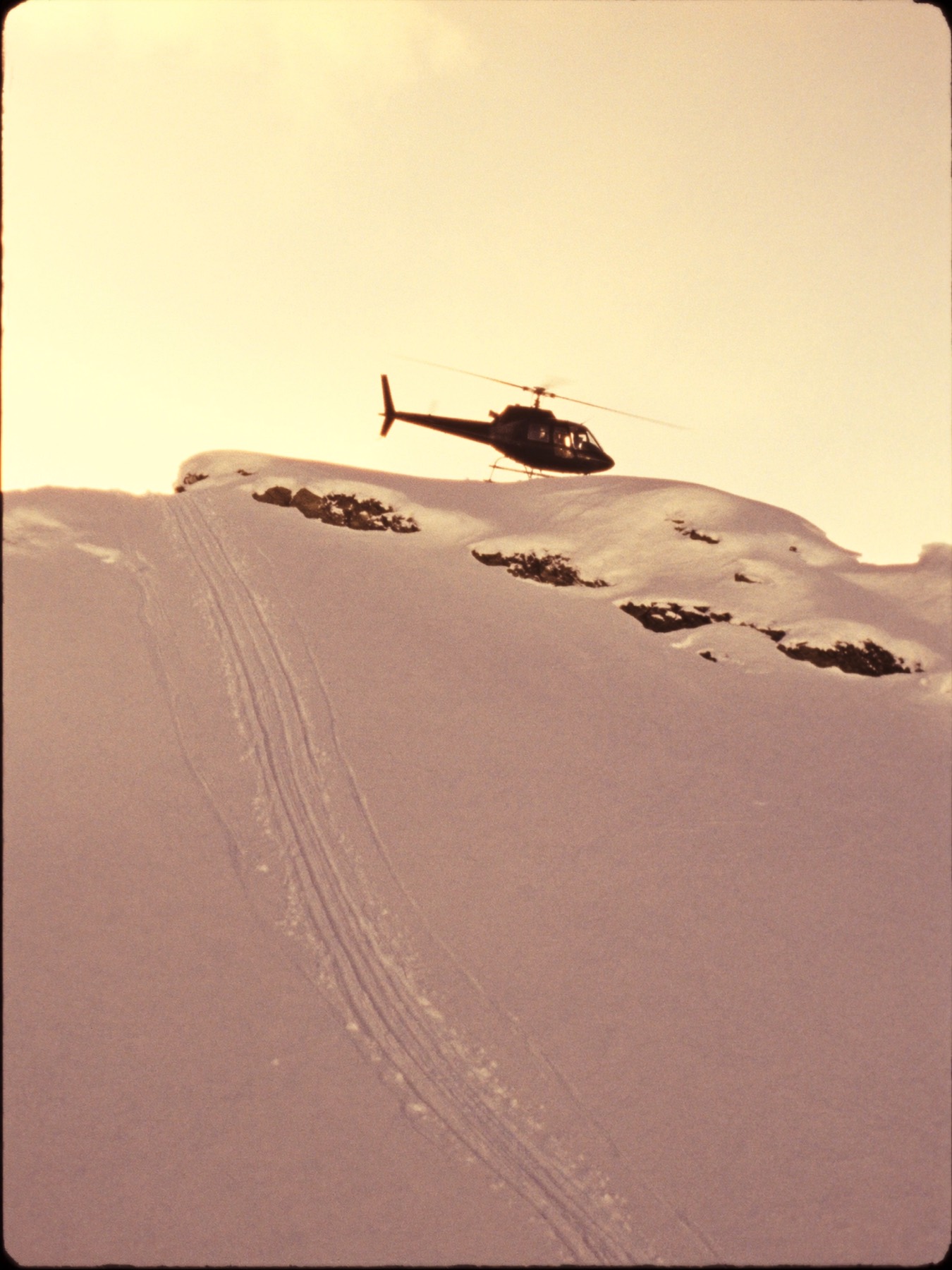 A helicopter resting on an untouched snow ridge at dawn